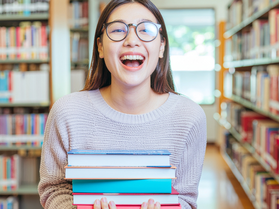 Excited teen in library holding books